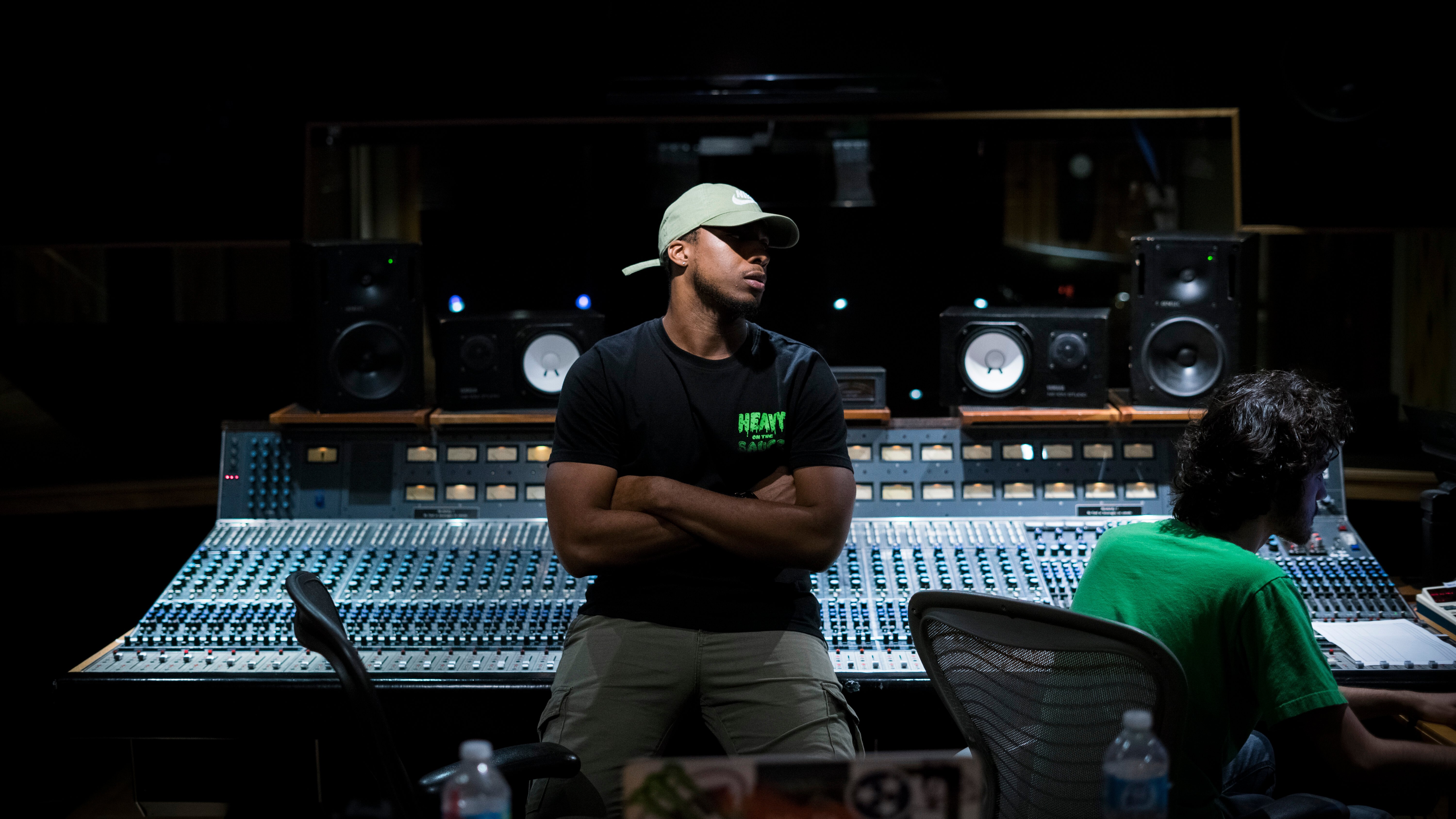 Gee Smiff sits in front of a large sound board in his production studio, creating music for sync licensing deals.