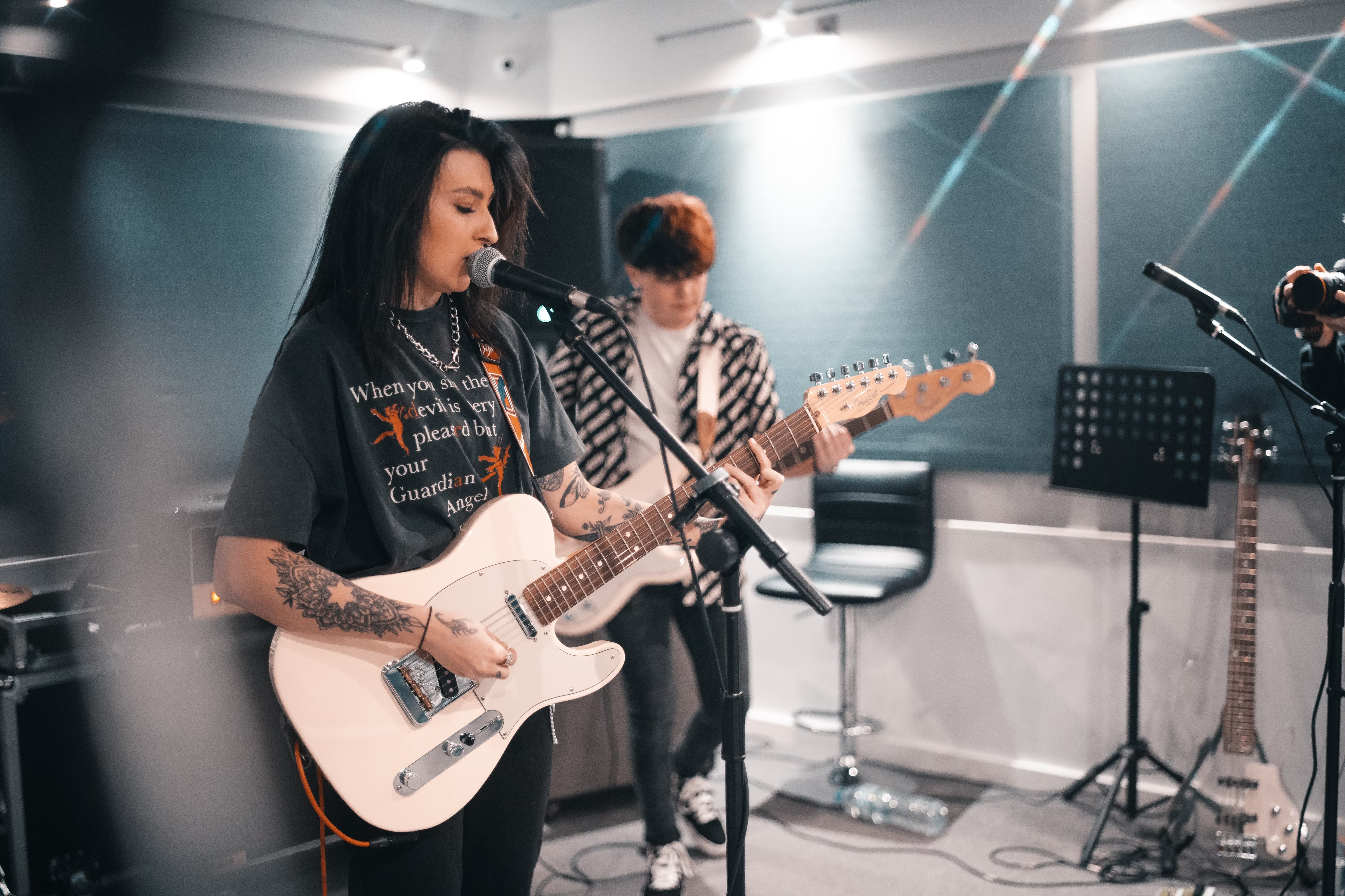 Two people playing electric guitar and singing into a microphone to create their master recording